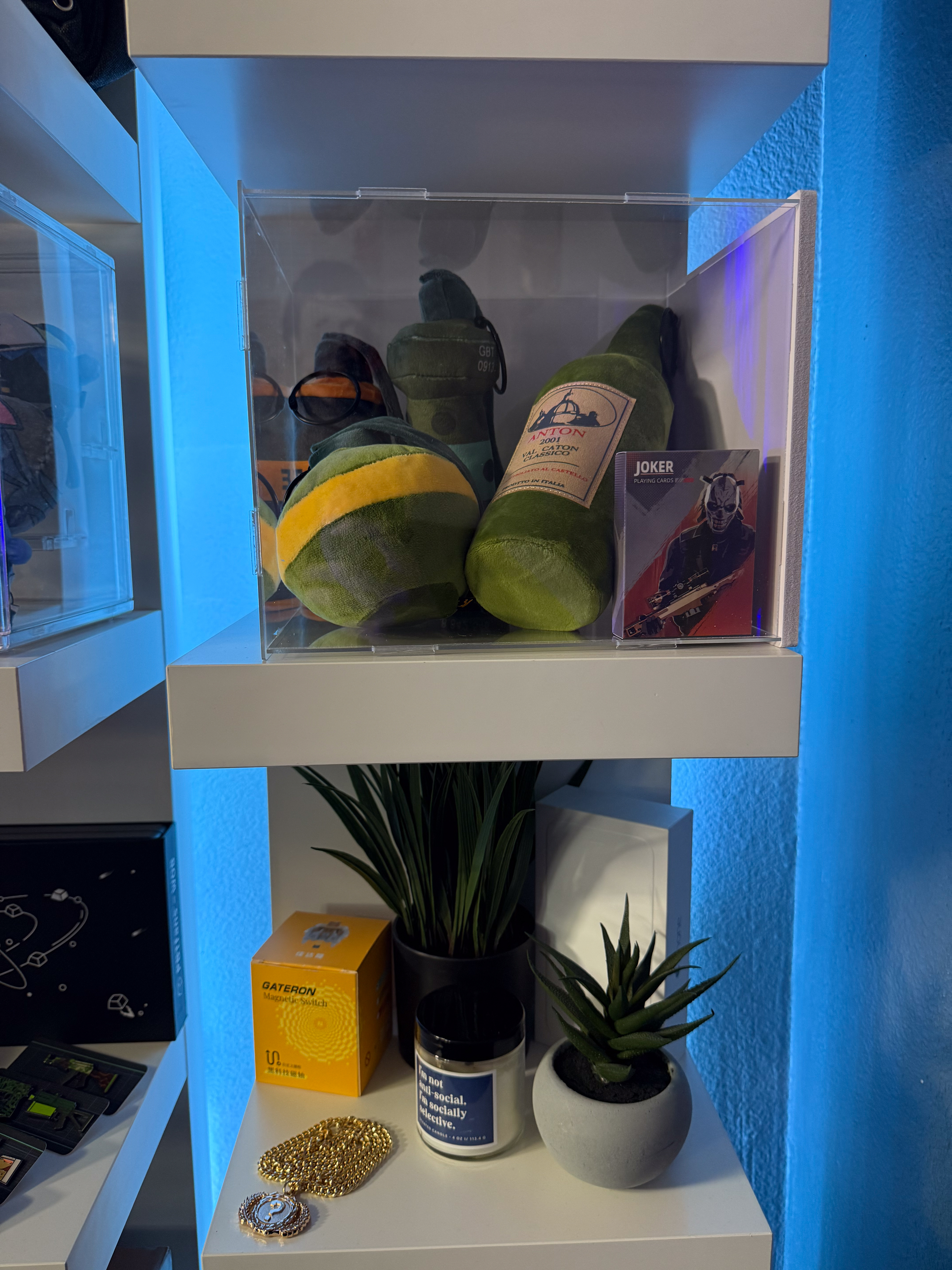 PGL Shangahi grenade plushies on and playing card on top shelfe. Gold chain from pgl shanghai on bottom shelf with fake platns, candle, gateron magnetic jade box